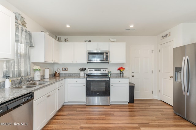 kitchen featuring light wood-style flooring, a sink, visible vents, white cabinetry, and appliances with stainless steel finishes