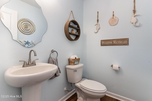 bathroom featuring toilet, a sink, baseboards, and wood finished floors