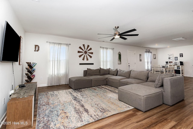 living area with a ceiling fan, visible vents, baseboards, and wood finished floors