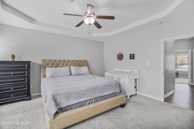 carpeted bedroom featuring baseboards, a raised ceiling, and a ceiling fan