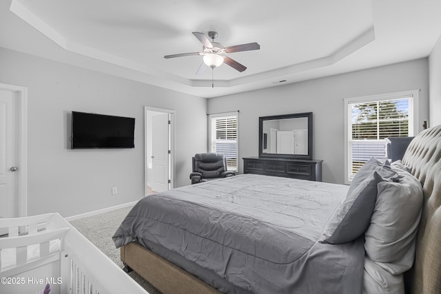 carpeted bedroom featuring a tray ceiling, ceiling fan, and baseboards