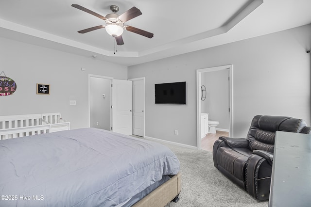 bedroom featuring a raised ceiling, light colored carpet, connected bathroom, ceiling fan, and baseboards