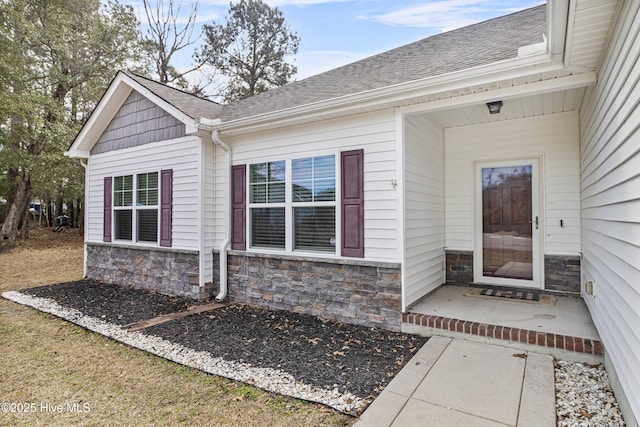 view of exterior entry with stone siding and roof with shingles