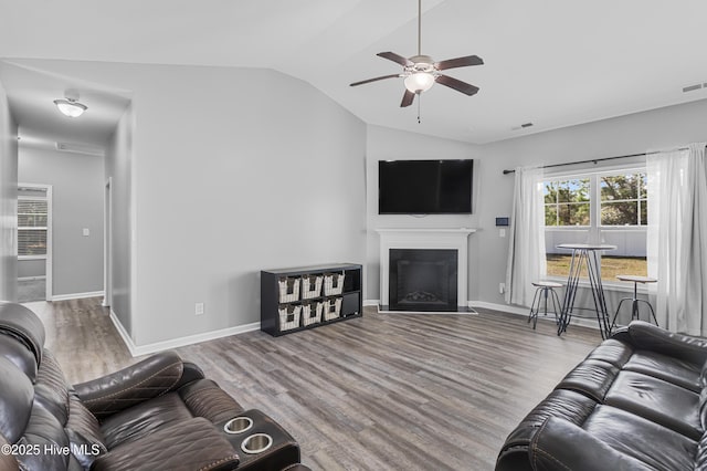 living area with lofted ceiling, a fireplace with flush hearth, baseboards, and wood finished floors