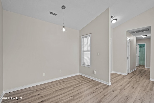 unfurnished room featuring lofted ceiling, light wood-style flooring, visible vents, and baseboards