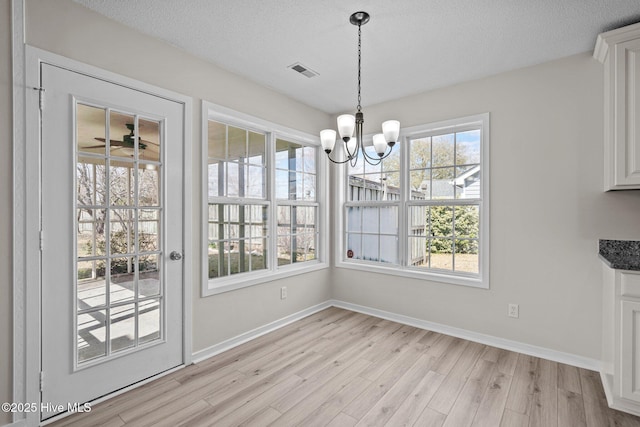 unfurnished dining area featuring a textured ceiling, light wood finished floors, a chandelier, and baseboards