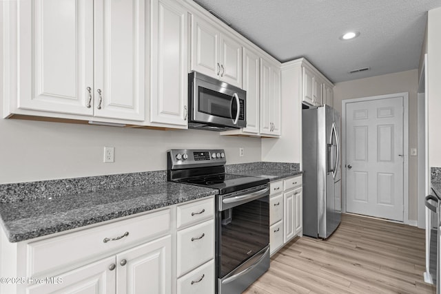 kitchen featuring light wood-type flooring, white cabinetry, stainless steel appliances, and a textured ceiling