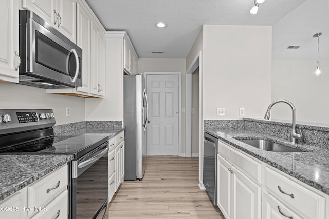 kitchen featuring stone counters, light wood-style flooring, appliances with stainless steel finishes, white cabinetry, and a sink