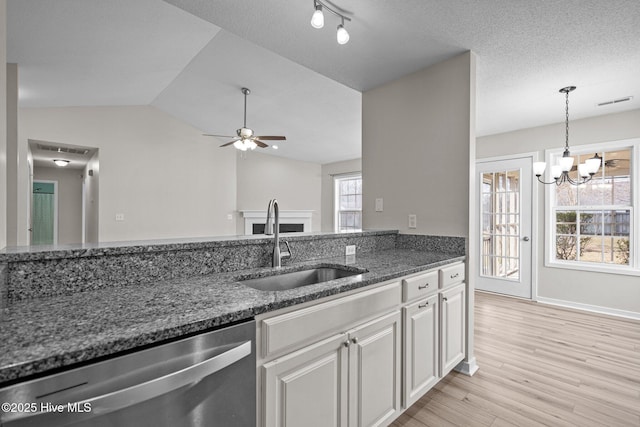 kitchen featuring dark stone counters, vaulted ceiling, a sink, light wood-type flooring, and dishwasher