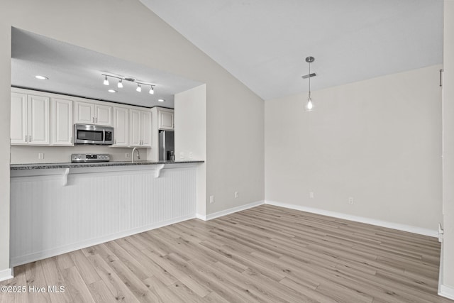 kitchen featuring light wood finished floors, lofted ceiling, a breakfast bar area, appliances with stainless steel finishes, and a sink