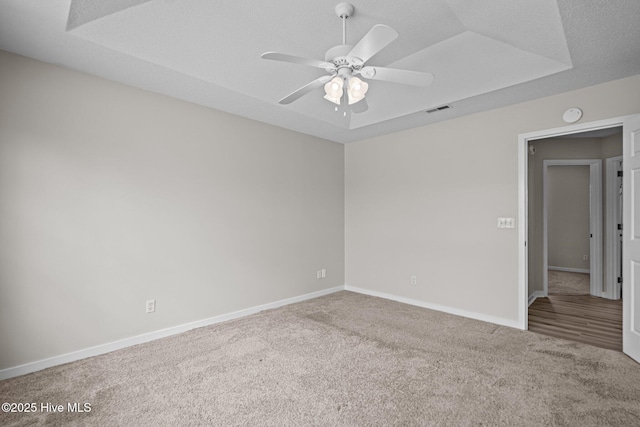 unfurnished room featuring a ceiling fan, a tray ceiling, carpet flooring, and baseboards