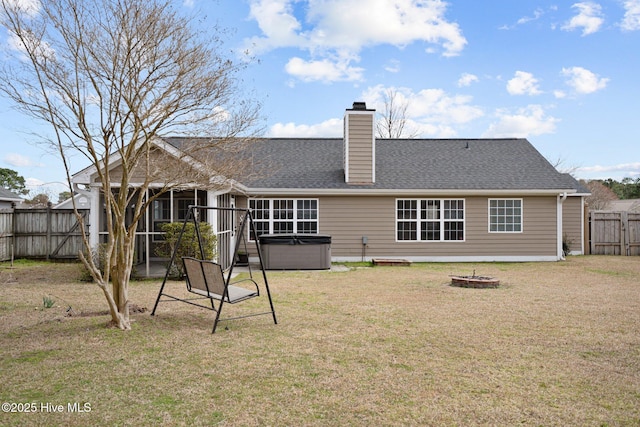 rear view of house with a yard, a chimney, a hot tub, fence, and a fire pit