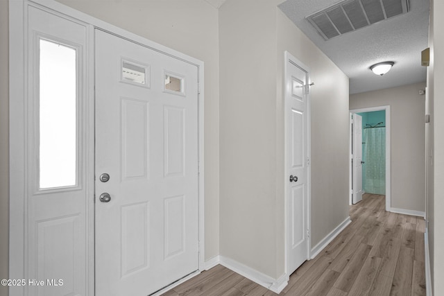 entryway with light wood-style floors, baseboards, visible vents, and a textured ceiling