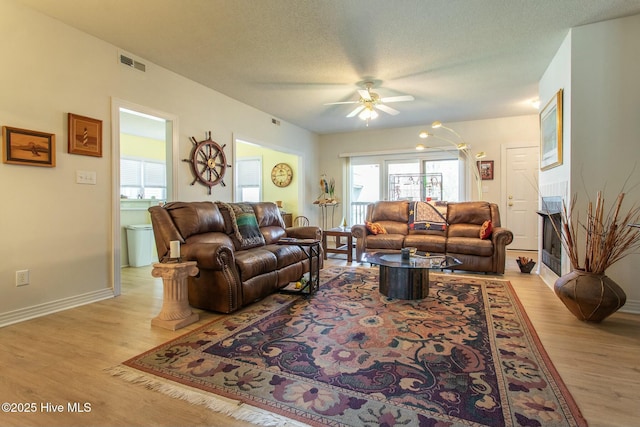 living room with baseboards, visible vents, light wood-style flooring, and a textured ceiling