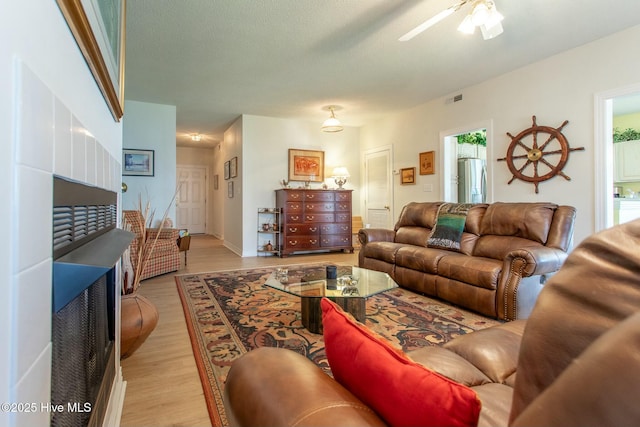 living area featuring light wood-type flooring, visible vents, ceiling fan, and a textured ceiling