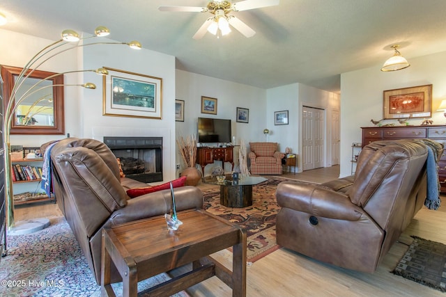 living room with a ceiling fan, a fireplace, and light wood finished floors