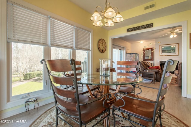 dining space featuring ceiling fan with notable chandelier, visible vents, baseboards, and wood finished floors