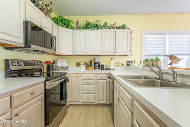 kitchen featuring stainless steel appliances, light wood-type flooring, light countertops, and a sink