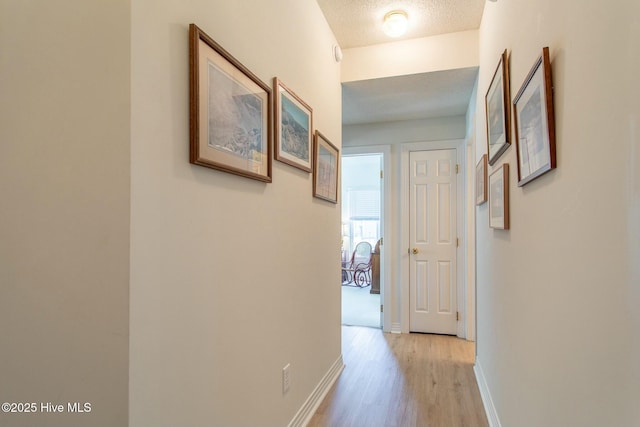 corridor featuring a textured ceiling, light wood-style floors, and baseboards