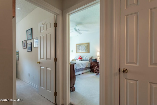 corridor with baseboards and light colored carpet