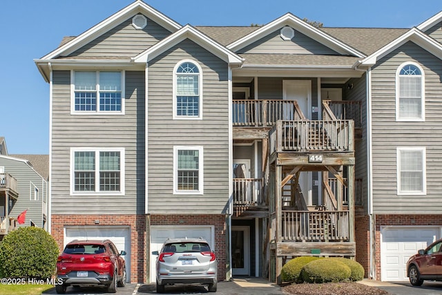 view of property featuring driveway, an attached garage, stairs, and brick siding