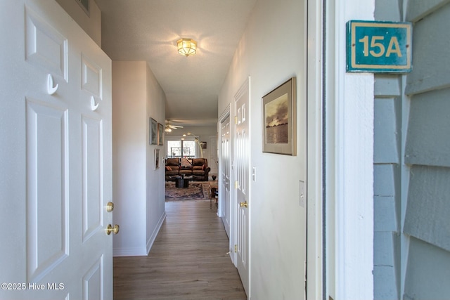 hallway featuring visible vents, baseboards, and wood finished floors