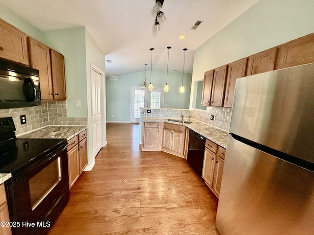 kitchen featuring pendant lighting, black appliances, wood finished floors, a peninsula, and vaulted ceiling