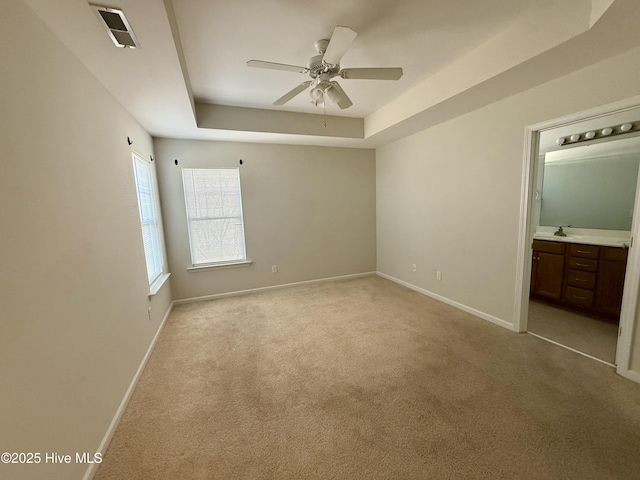 unfurnished bedroom featuring baseboards, visible vents, a tray ceiling, a sink, and light carpet