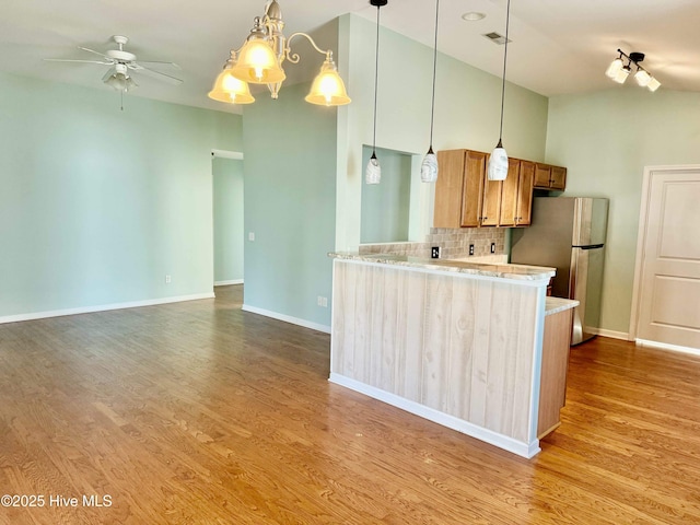 kitchen with tasteful backsplash, hanging light fixtures, freestanding refrigerator, wood finished floors, and brown cabinetry