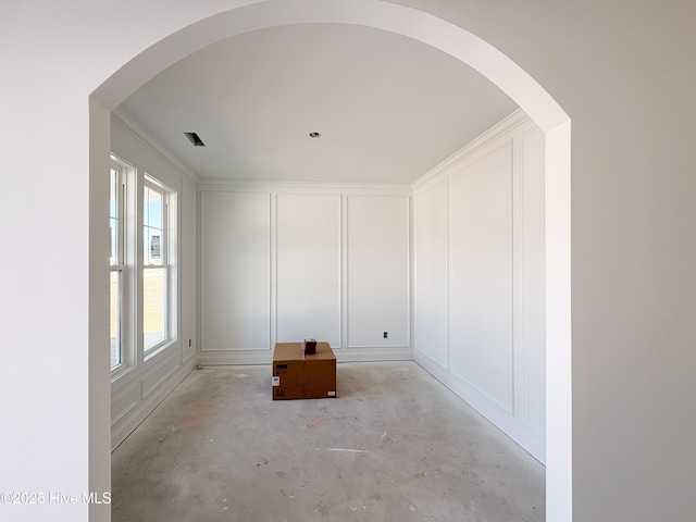 empty room with arched walkways, a decorative wall, and concrete flooring