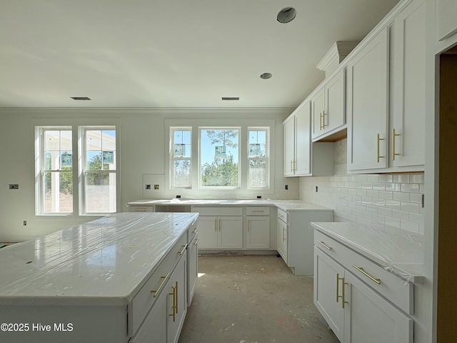 kitchen with light stone countertops, white cabinets, crown molding, tasteful backsplash, and a center island