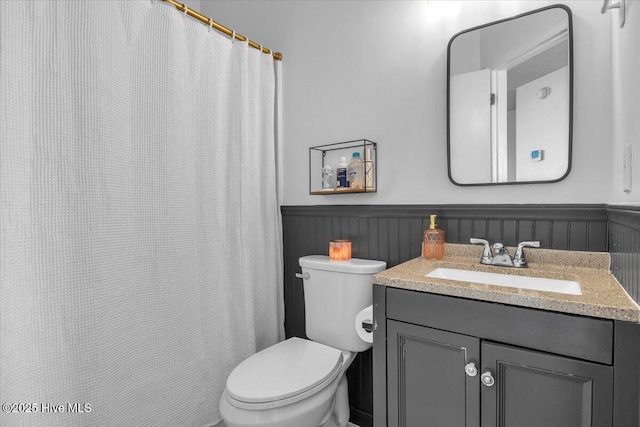 bathroom with a wainscoted wall, vanity, and toilet