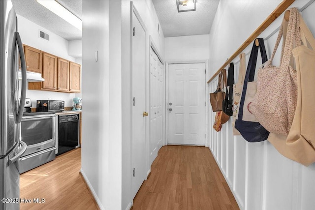 hall featuring light wood-style flooring, visible vents, and a textured ceiling