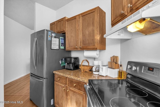 kitchen featuring baseboards, appliances with stainless steel finishes, brown cabinets, wood finished floors, and under cabinet range hood