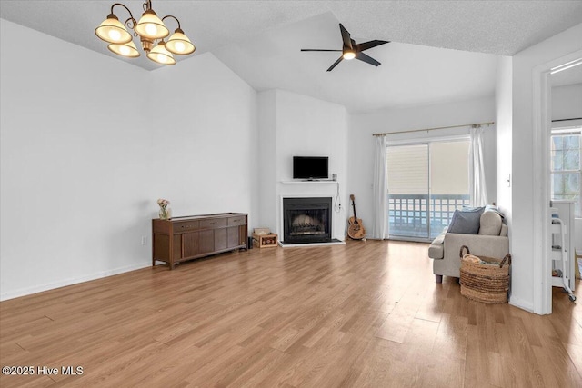 living area featuring lofted ceiling, ceiling fan with notable chandelier, a fireplace, baseboards, and light wood finished floors