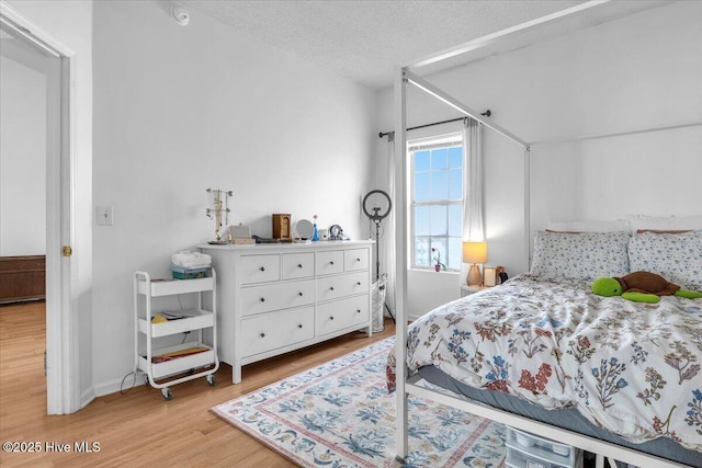 bedroom with a textured ceiling, light wood-style flooring, and baseboards