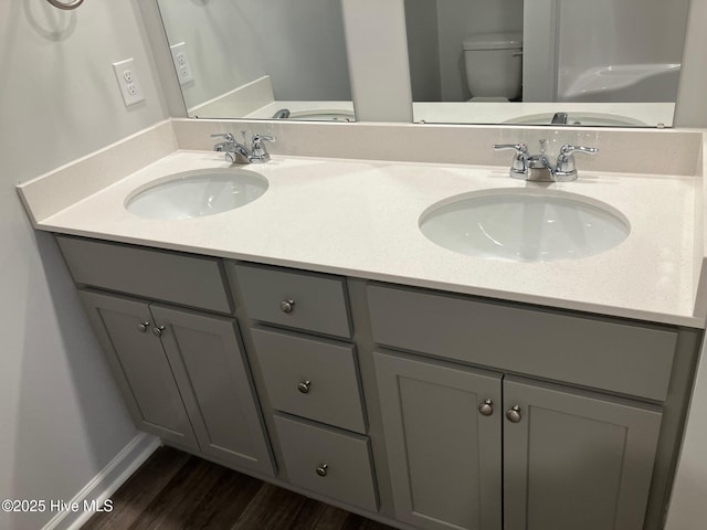 bathroom featuring double vanity, toilet, wood finished floors, and a sink