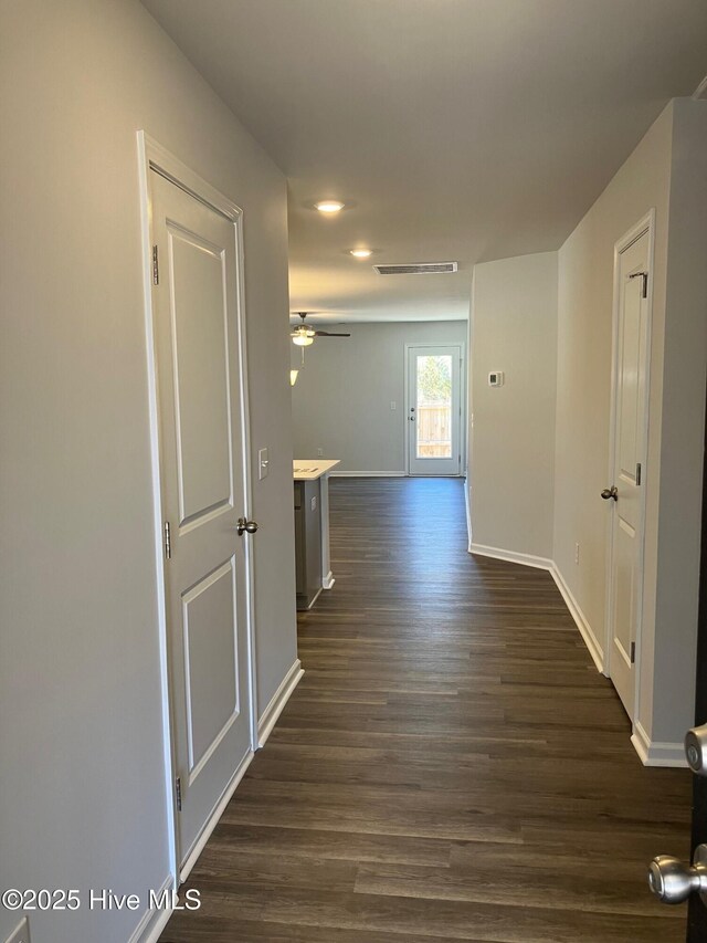 corridor featuring dark wood-type flooring, baseboards, and visible vents