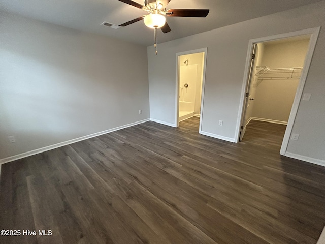 unfurnished bedroom with dark wood-type flooring, a spacious closet, baseboards, and a closet