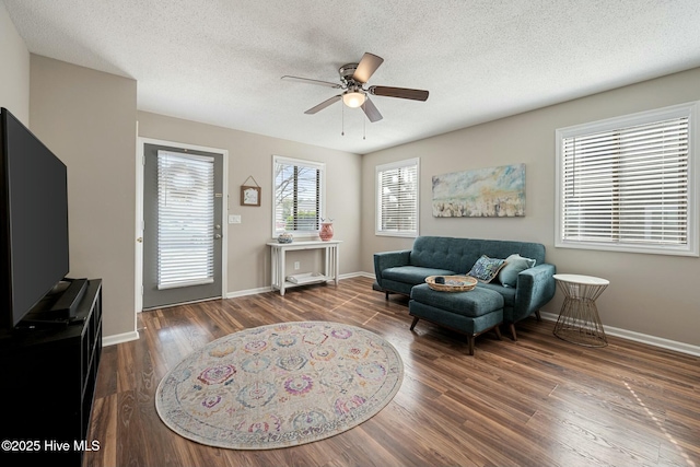 living area featuring baseboards, a textured ceiling, a ceiling fan, and wood finished floors