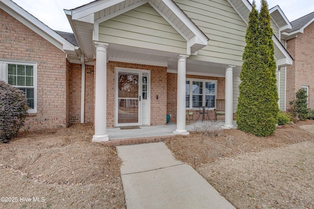 view of exterior entry with a porch and brick siding