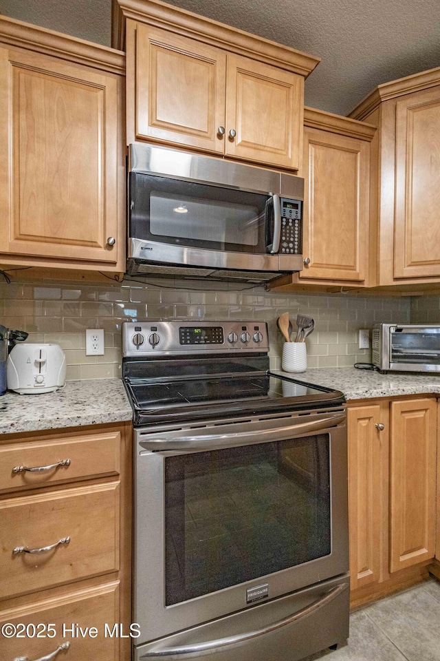 kitchen with light tile patterned floors, tasteful backsplash, a toaster, light stone counters, and stainless steel appliances