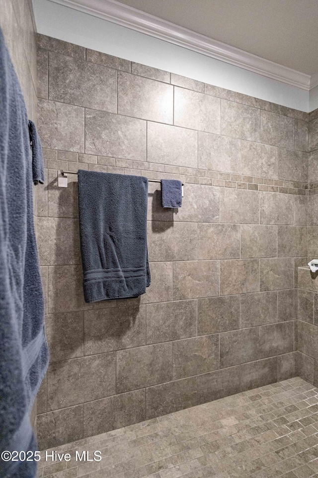 bathroom with ornamental molding and a tile shower