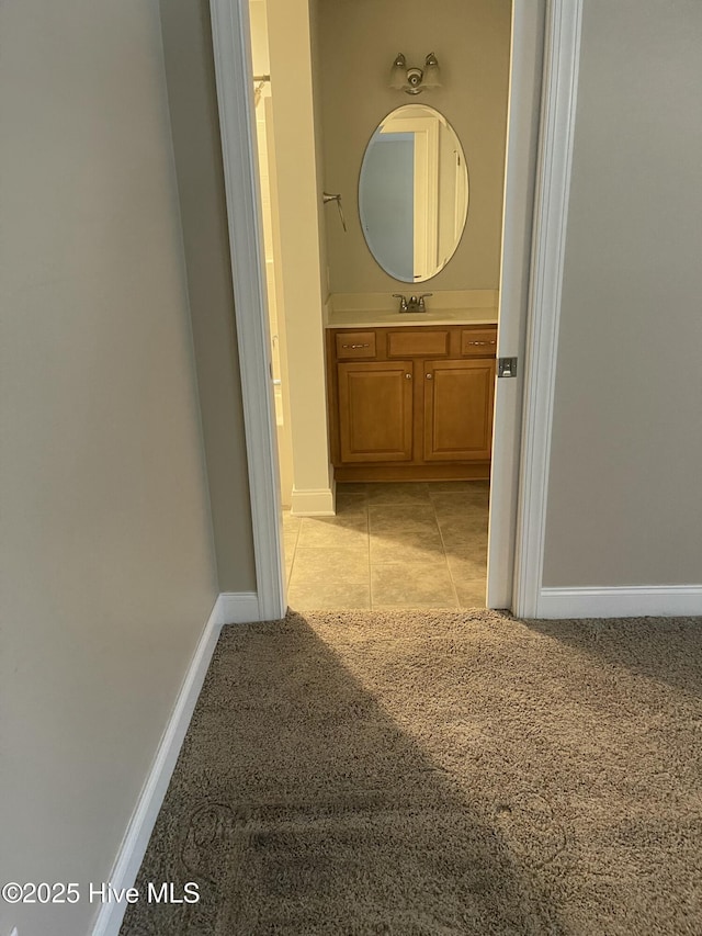 hallway with light tile patterned flooring, baseboards, light carpet, and a sink