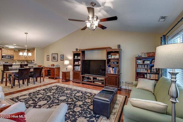 living room with lofted ceiling, light wood-style flooring, ceiling fan with notable chandelier, visible vents, and baseboards