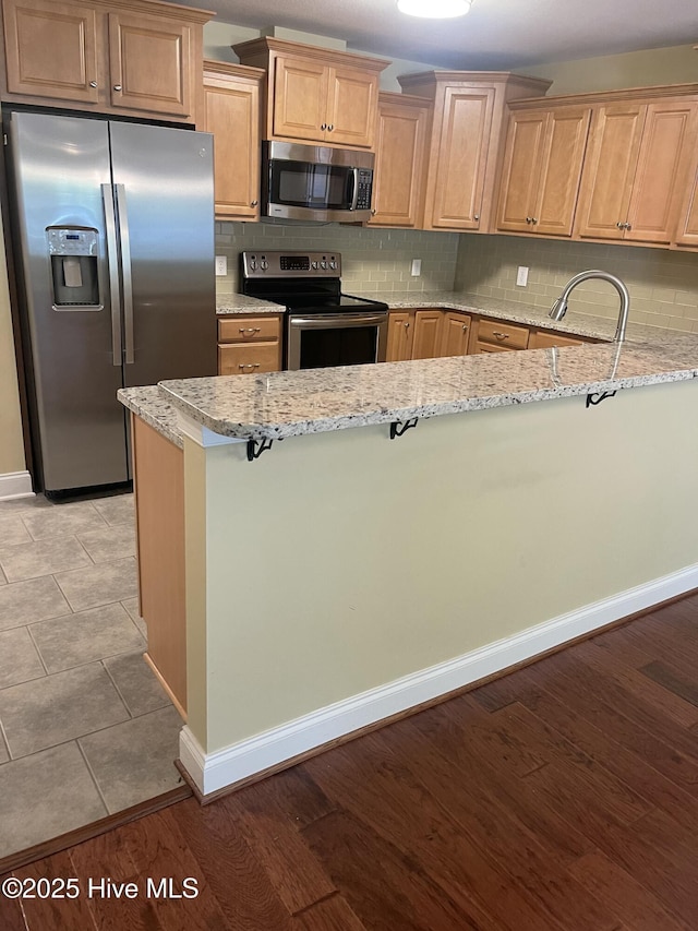kitchen featuring a peninsula, baseboards, tasteful backsplash, light stone counters, and stainless steel appliances
