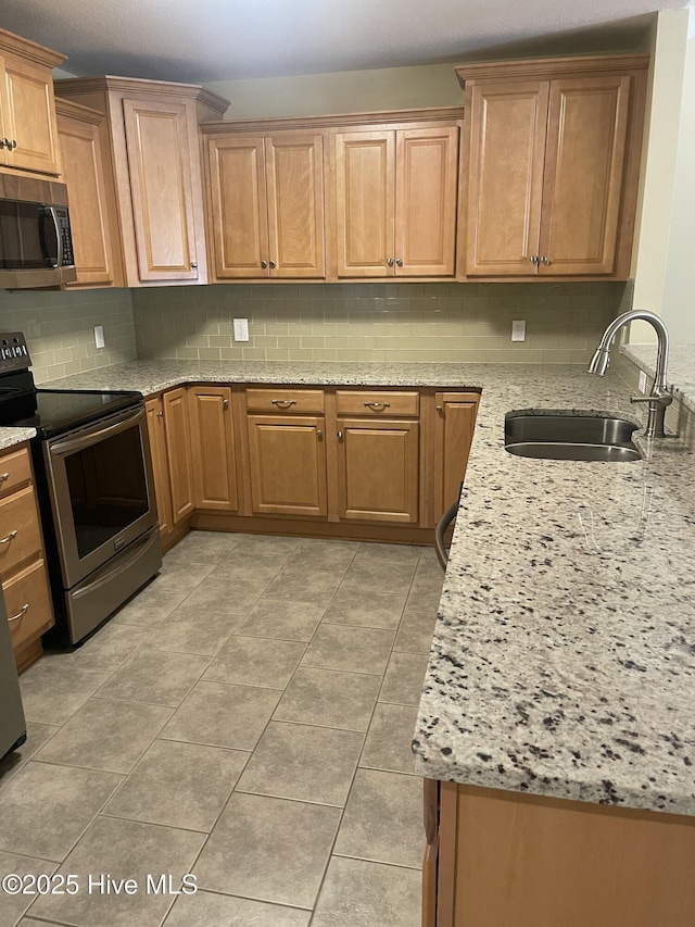 kitchen featuring tasteful backsplash, light stone countertops, a sink, light tile patterned floors, and stainless steel appliances