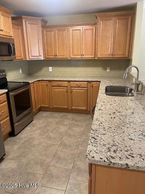 kitchen featuring decorative backsplash, light stone counters, a sink, appliances with stainless steel finishes, and light tile patterned floors