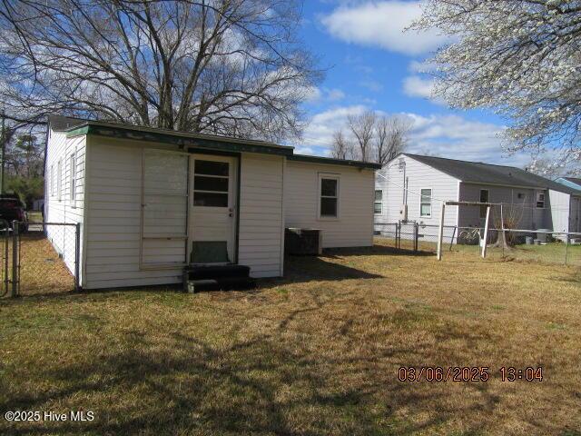 rear view of property with a lawn, an outdoor structure, and fence