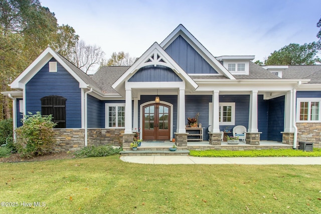 view of front of house with stone siding, a front yard, board and batten siding, and french doors